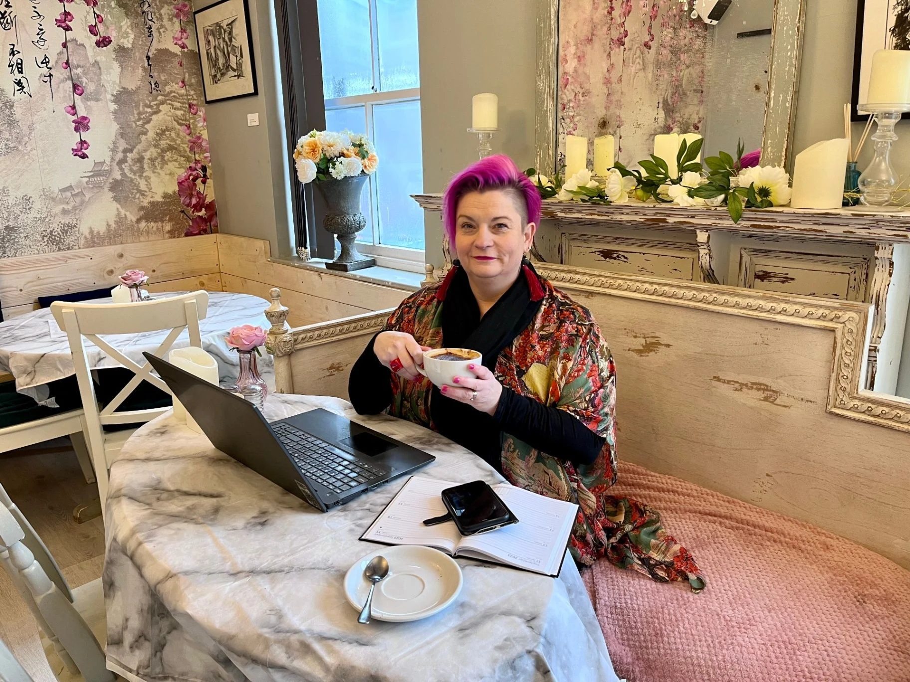 Belinda Warburton sitting at a table with a laptop, notebook and cup of coffee