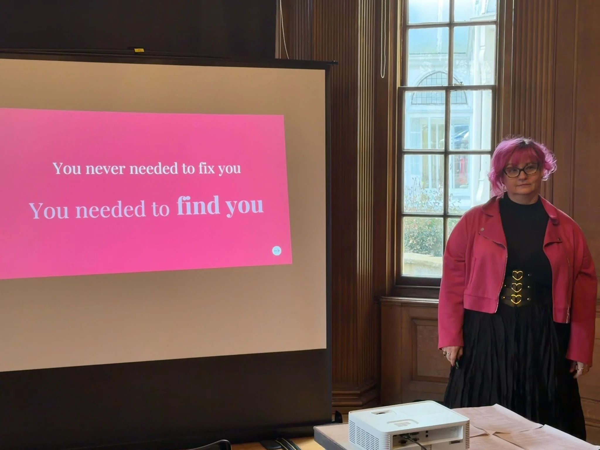 Belinda Warburton standing beside a presentation screen displaying the message ‘You never needed to fix you. You needed to find you.’